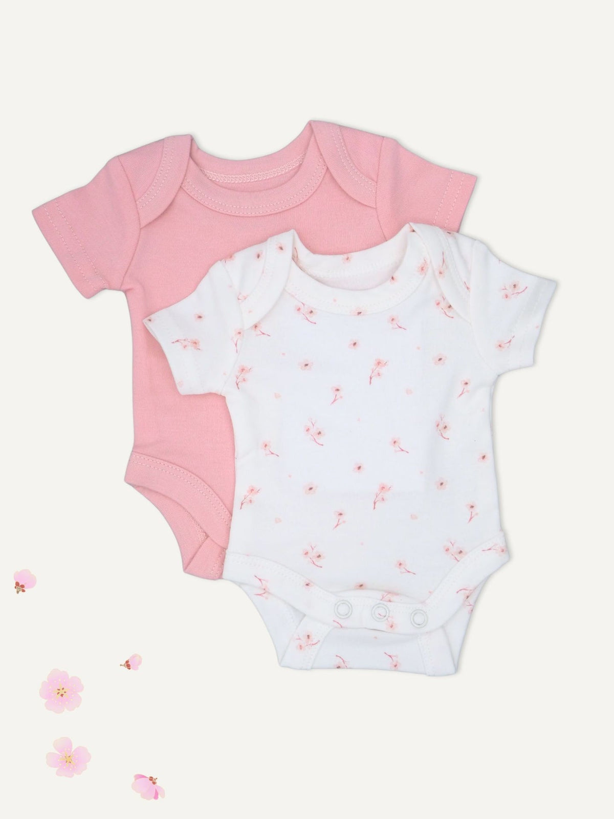 Two short-sleeve baby bodysuits laid flat on a light cream background: one solid light pink and one white with a scattered small pink floral print. No person, animal, or real environment is present.