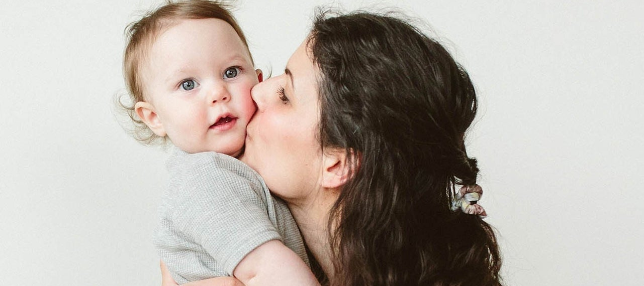 Woman kissing a baby on the cheek against a white background