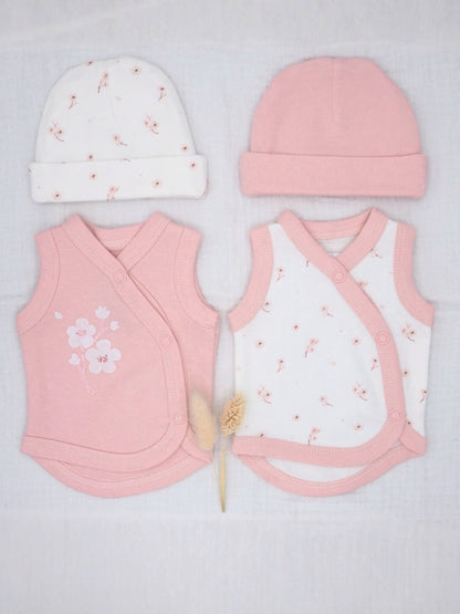 A baby clothing set laid flat on a white textured fabric background, including a pink knit hat, a white knit hat with small pink floral prints, a pink wrap vest, and a white wrap vest with pink trim and tiny pink floral prints. A small dried flower stem lies between the garments.